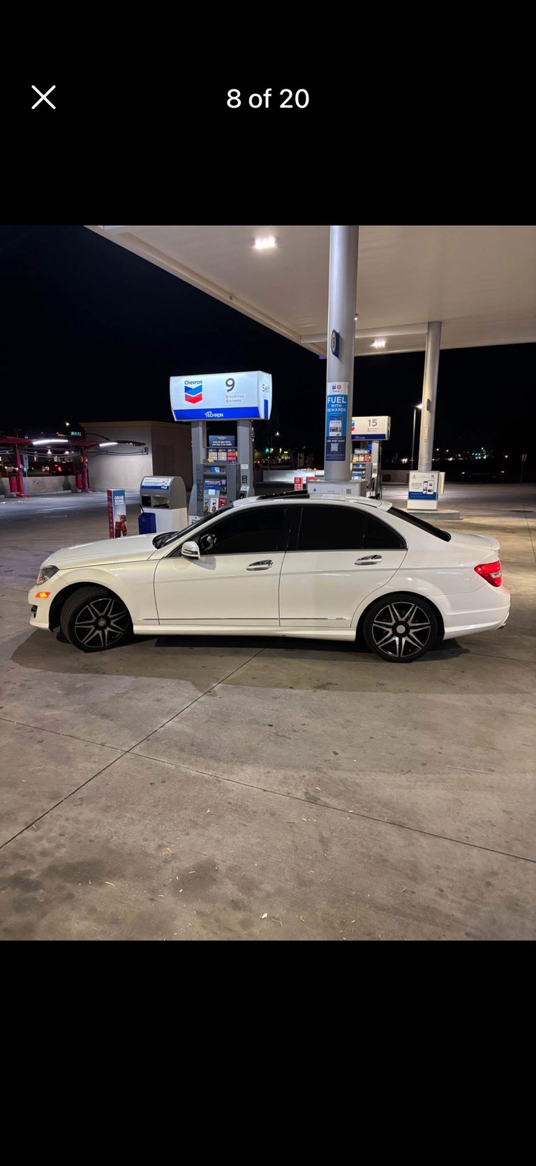 White sedan parked at night at a Chevron gas station with pump 9 visible in the background